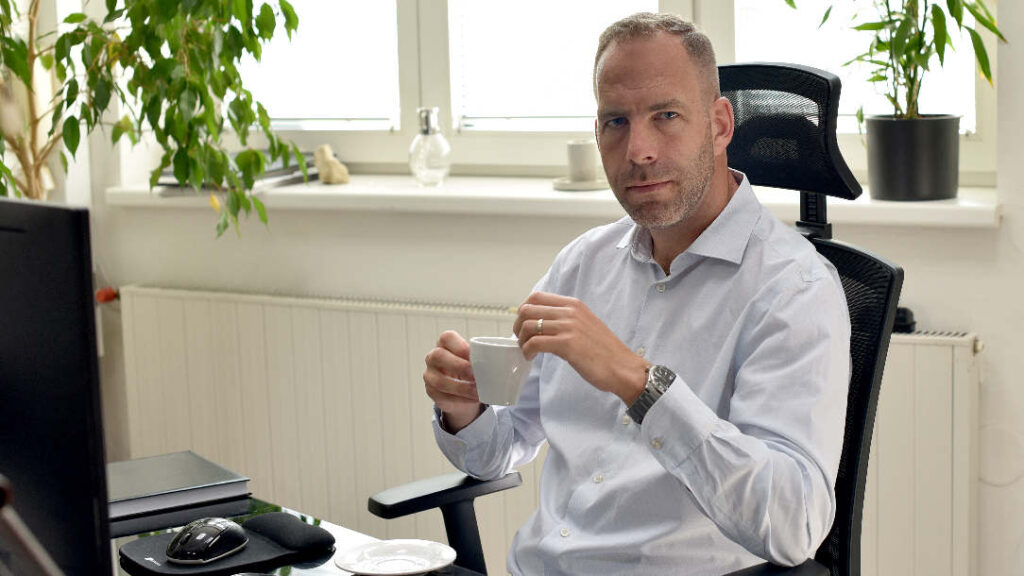 Petr v kanceláři v MADIO drží hrnek kávy a usmívá se - Petr Štěpáník